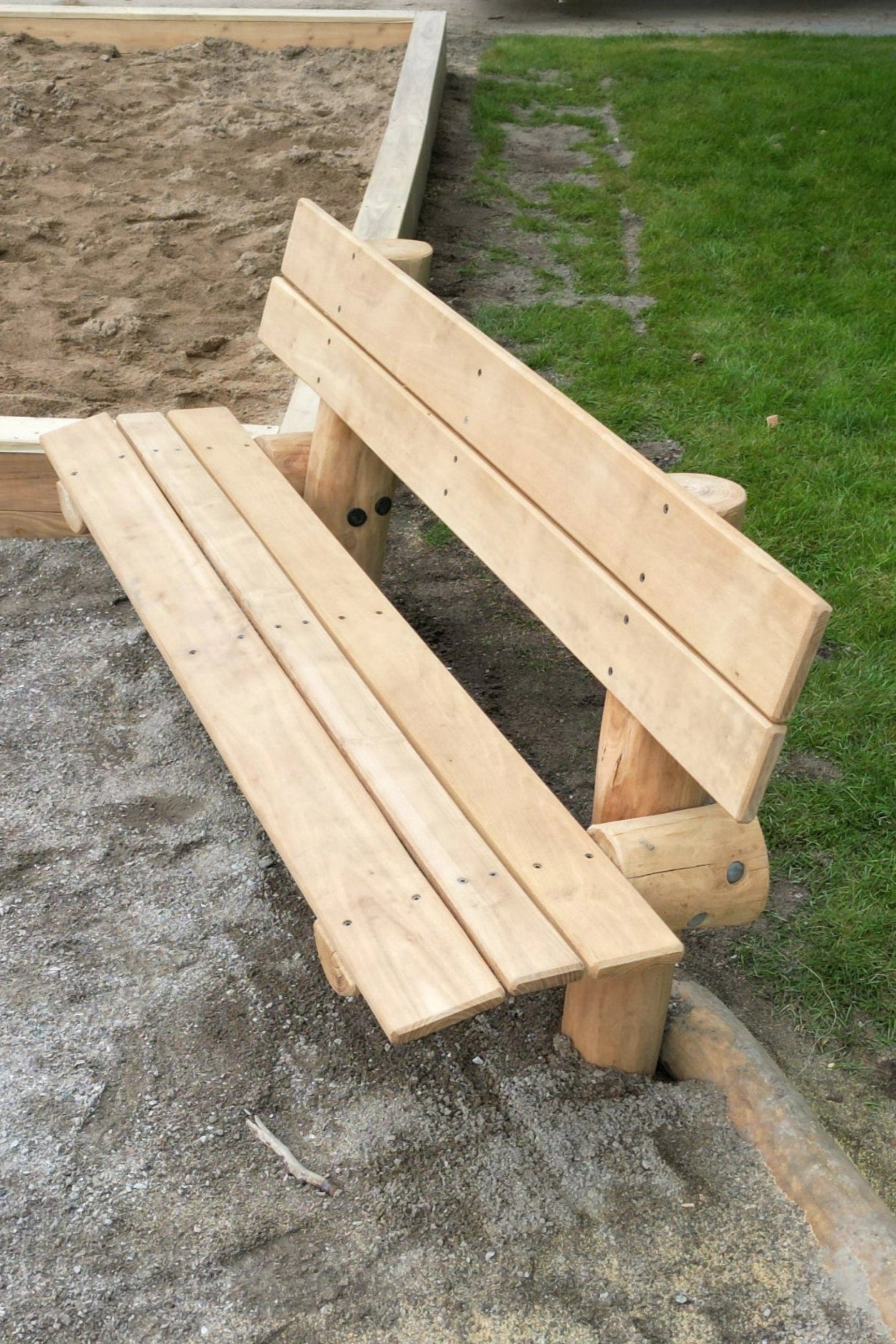 Robinia träbänk i en lekplark med gräs i bakgrunden.