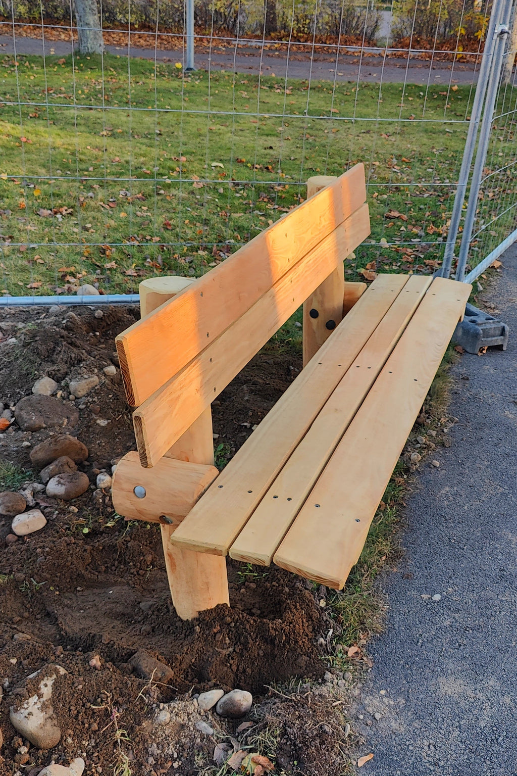 Robinia träbänk förankrad i marken vid en stig i en park